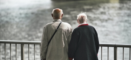 A couple of seniors holding hands on a bridge over a river