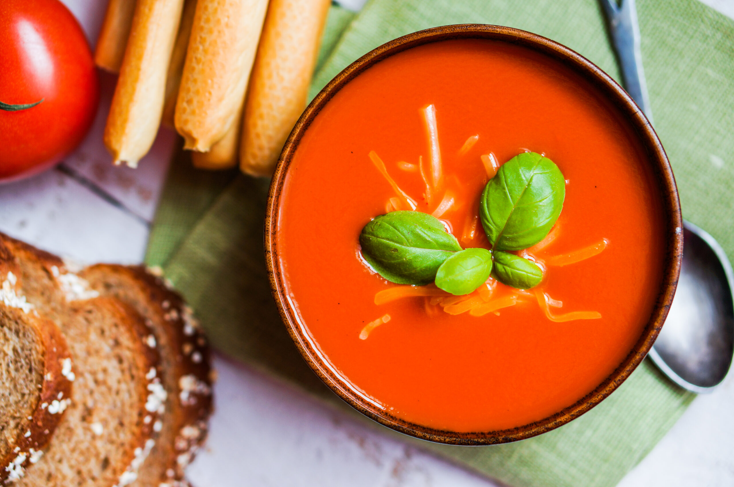 Tomatoe soup with bread sticks and basil on wooden background