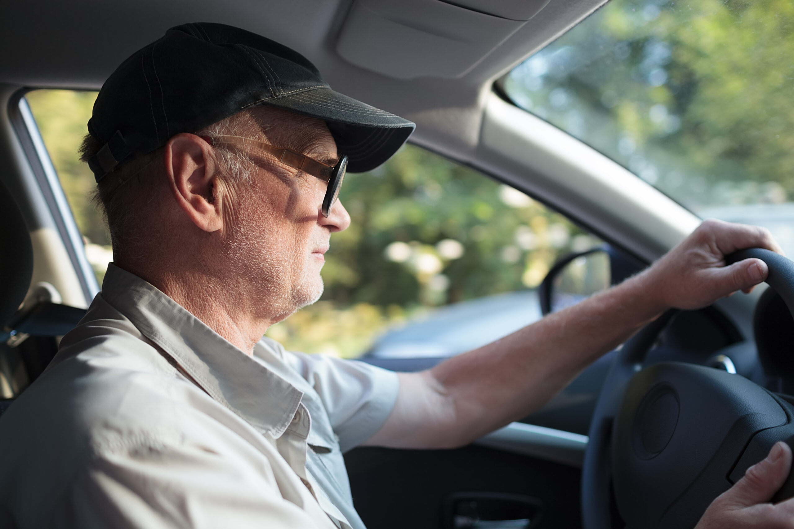 Side view of an elderly man in glasses driving a car on a sunny summer day